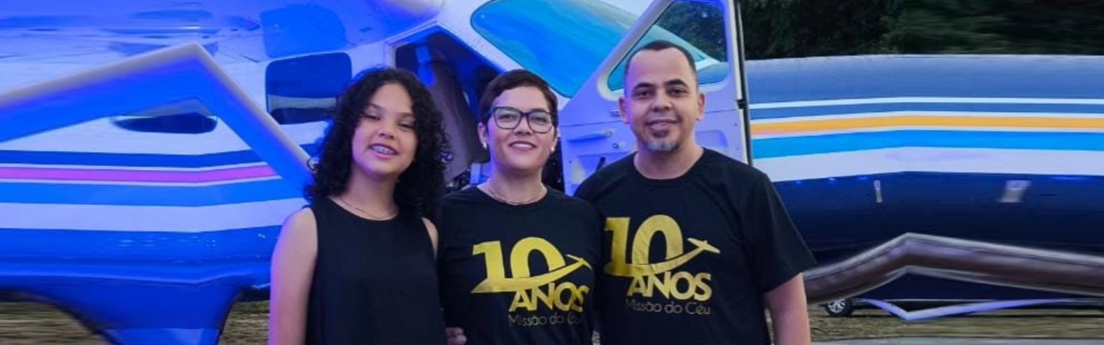 Família Teixeira em frente a uma aeronave, com camisetas de comemoração dos 10 anos da Missão do Céu